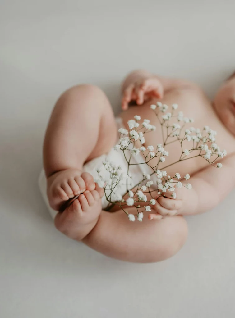 Baby hält eine weiße Blume mit seinen Füßen. Es interessiert sich zum ersten mal für ätherische Öle und deren Wirkung.