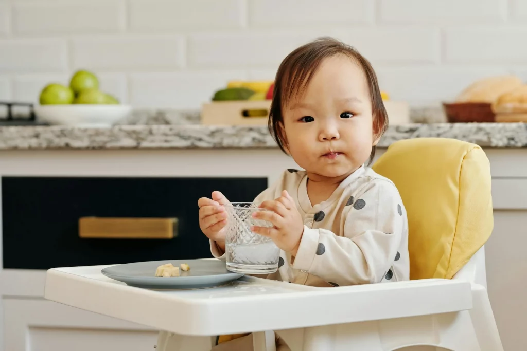 Baby hat beim Baby-Led Weaning seinen Teller aufgegessen und hält noch ein Glas Wasser in der Hand.