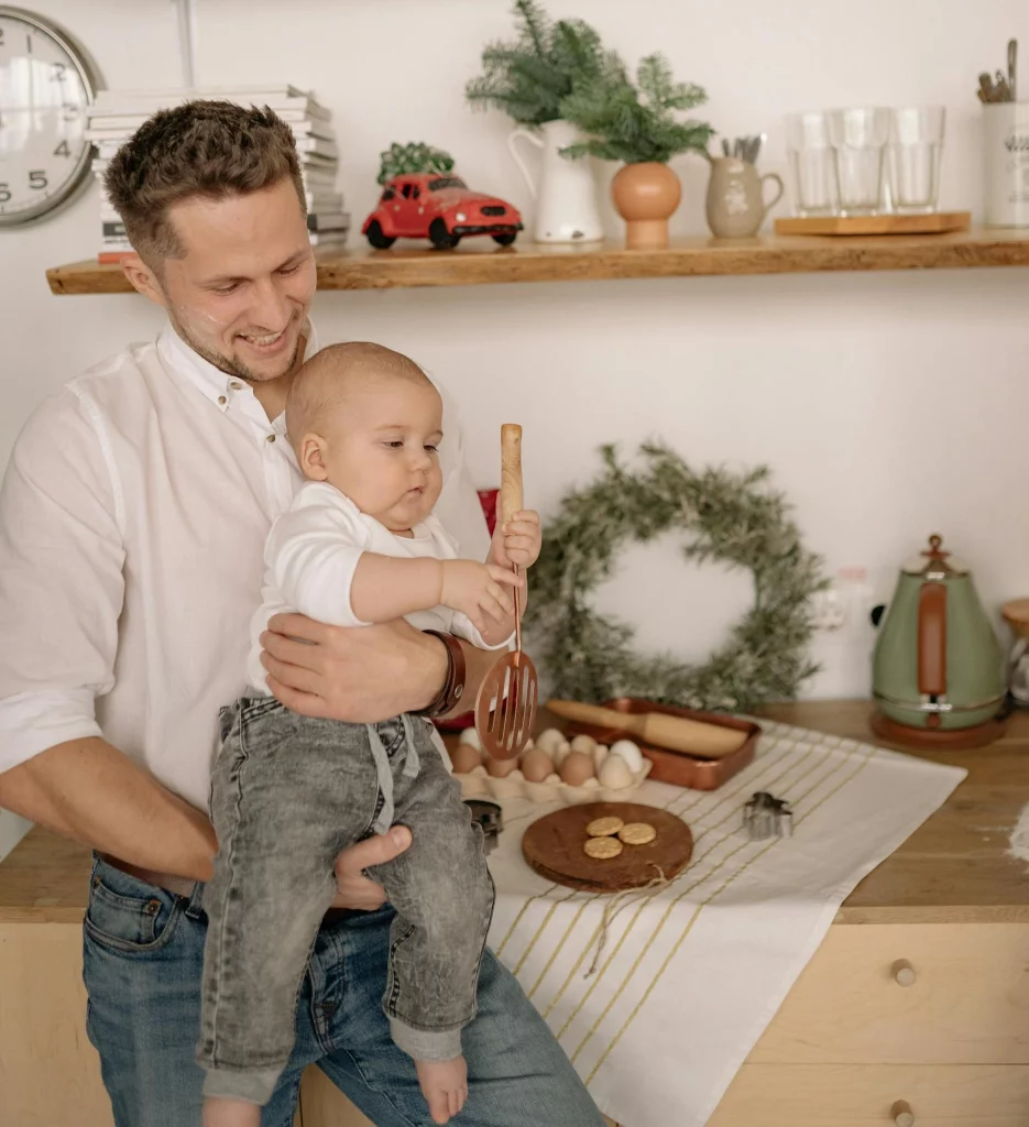 Vater hilft mit dem Baby im Wochenbett. Sie erledigen zusammen Arbeiten in der Küche.