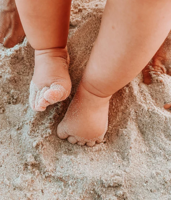 Baby vergräbt seine Füße im Urlaub im Sand